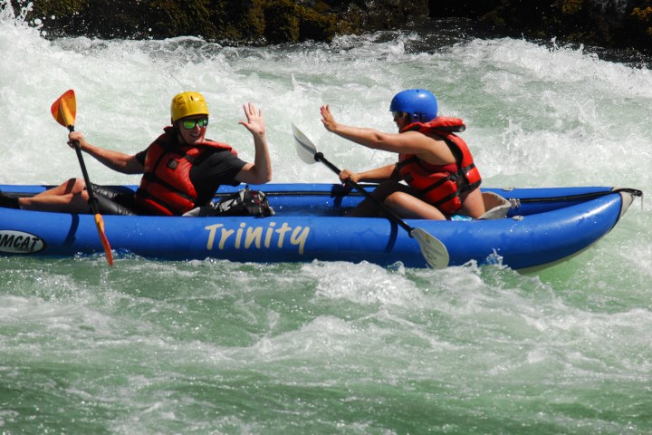 Two kayakers high-five on an inflatable tandem kayak