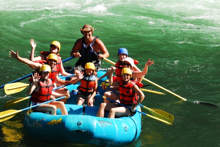 A rafting group smiles and waves from an inflatable raft